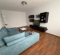 Nappali televízióval, kék kanapéval és fa dekorációjú padlóval egy háromszobás lakásban.