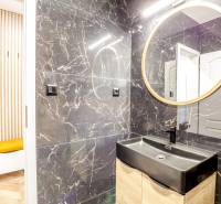 Fürdőszoba a nyaraló apartmanban fekete mosdóval és kerek tükörrel.