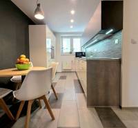 Konyha egy kétszobás lakásban étkezőasztallal, csempével és munkalap feletti világítással.