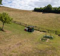 Dombos terep Banská Belá-ban lakóövezeti telkekkel, fiatal fákkal és kerttel.