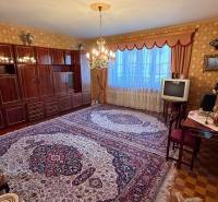 Nappali egy családi házban szőnyeggel, régebbi televízióval és elegáns csillárral.