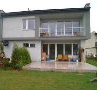 Családi ház Bystričkán, terasz ülőhellyel, nagy ablakokkal és rendezett gyep.