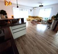 Nappali egy családi házban, fa mintázatú padlóval és világos kanapéval.