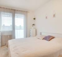 Hálószoba egy háromszobás lakásban világos ággyal és komóddal, növénnyel díszítve.