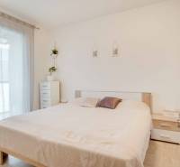 Világos hálószoba egy háromszobás lakásban fehér bútorokkal és ággyal.