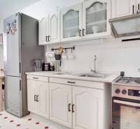 Konyha egy háromszobás lakásban fehér szekrényekkel, tűzhellyel és nagy hűtőszekrénnyel.