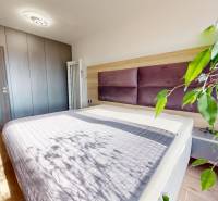 Hálószoba egy háromszobás lakásban fa dekorú padlóval, nagy ággyal és növénnyel.