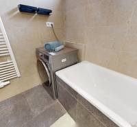 Fürdőszoba egy háromszobás lakásban káddal, mosógéppel és törölközőkkel a bézs csempéken.