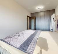 Hálószoba nagy ággyal, beépített szekrénnyel és fa dekorációjú padlóval egy háromszobás lakásban.