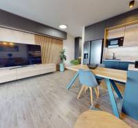 Nappali egy háromszobás lakásban fa dekor padlóval és konyhával.