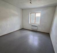 Fehér falú, szürke padlójú és kis ablakú szoba a gyártóhelyiségben.