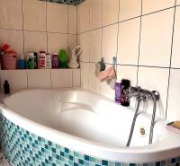 Fürdőszoba sarokkáddal és kék-fehér csempével egy kétszobás lakásban.