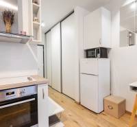 Kompakt konyha főzőlappal, hűtőszekrénnyel és fa dekor padlóval egy egyszobás lakásban.