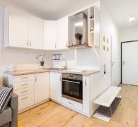 Konyha fehér szekrényekkel egy egyszobás lakásban és fa mintázatú padlóval.