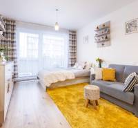 Egyszobás lakás fa dekor padlóval, ággyal, kanapéval és sárga szőnyeggel.