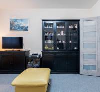 Nappali egy négyszobás lakásban sötét bútorokkal, televízióval és vitrinel.