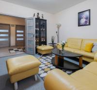 Nappali egy négy szobás lakásban sárga bőrkanapéval, üveg vitrin és képpel a falon.