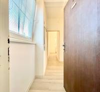 Folyosó fa hatású padlóval, fehér falakkal, nagy ablakkal és redőnyökkel.