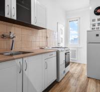 Kuchyňa v 1-izbovom byte s podlahou s dreveným dekorom a bielymi skrinkami.