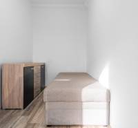 Úzka miestnosť s posteľou a komodou, podlaha s dreveným dekorom, 1-izbový byt.