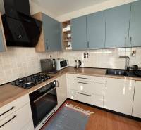 Konyha egy háromszobás lakásban csempézett burkolattal és fa mintázatú padlóval.