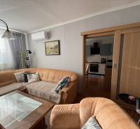 Nappali kanapéval, üvegasztallal és konyhával egy háromszobás lakásban.