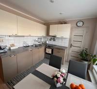 Konyha egy háromszobás lakásban világos szekrényekkel és étkezőasztallal.