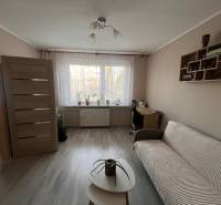 Nappali egy háromszobás lakásban fa mintázatú padlóval, kanapéval és asztallal.