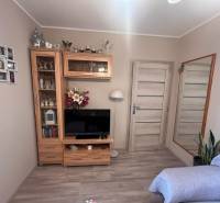 Szoba televízióval, tükörrel, fa bútorzattal és kanapéval, egy háromszobás lakásban.