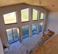 Egy kunyhó belseje nagy ablakokkal, lépcsőkkel és fa dekorációjú padlóval.