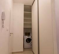 Egy szűk folyosó egy egyszobás lakásban mosógéppel és tolóajtókkal.