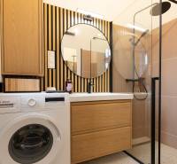 Fürdőszoba mosógéppel, mosdóval, tükörrel és zuhanyzóval egy háromszobás lakásban.