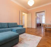 Szoba egy háromszobás lakásban kék kanapéval, fa dekorációjú padlóval és étkező sarokkal.