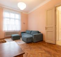 Világos nappali kanapéval, csillárral és fa dekorációjú padlóval egy háromszobás lakásban.