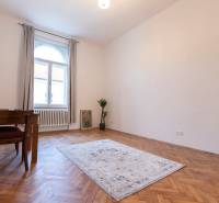 Szoba egy háromszobás lakásban, fa dekorációjú padlóval, szőnyeggel és asztallal.