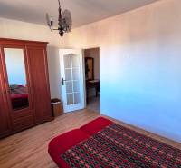 Hálószoba egy kétszobás lakásban fa hatású padlóval, szekrénnyel és ággyal.