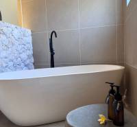 Fürdőszoba családi házban káddal, kővel burkolt fallal és dekoratív üvegcsékkel.