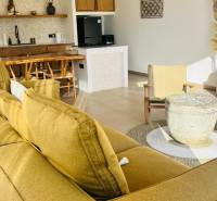 Családi ház belső tere kanapéval, konyhával, rattan székekkel és természetes anyagokból készült kiegészítőkkel.