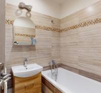 Fürdőszoba egy kétszobás lakásban világos csempékkel és káddal, mosdó alatti szekrényekkel.