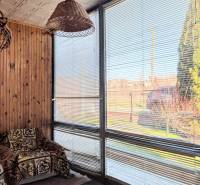 Családi ház rattan lámpával, takaróval borított székkel és redőnyös ablakokkal.