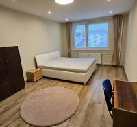 Világos szoba egy kétszobás lakásban ággyal és bútorokkal, fa dekorációjú padlóval.