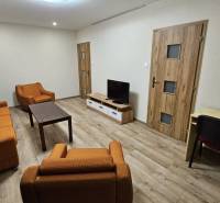 Nappali egy kétszobás lakásban narancssárga bútorokkal és fa dekorációjú padlóval.