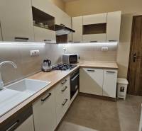 Konyha egy kétszobás lakásban fehér szekrényekkel és fa dekor padlóval.