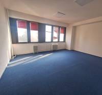 Iroda kék szőnyeggel és nagy ablakokkal, világos tér.