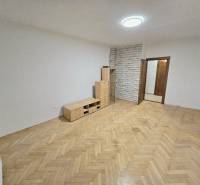 Világos szoba egy kétszobás lakásban, fa dekoros padlóval és bútorokkal.