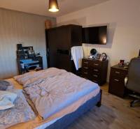 Hálószoba egy háromszobás lakásban, kényelmes ággyal, íróasztallal és fa dekorációjú padlóval.