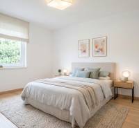 Világos hálószoba fa dekor padlóval, világos ágytakaróval ellátott ágy és képek a falon.