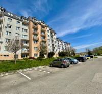 Konténerház a Východná utcán, parkoló, fák, 2 szobás lakás, kék ég, autó.