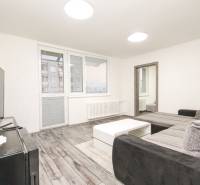 Nappali szoba fa dekoros padlóval, kanapéval és asztallal egy háromszobás lakásban.