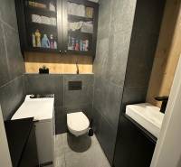 Fürdőszoba WC-vel egy kétszobás lakásban, csempék, szekrény, mosógép és tárolóhely.